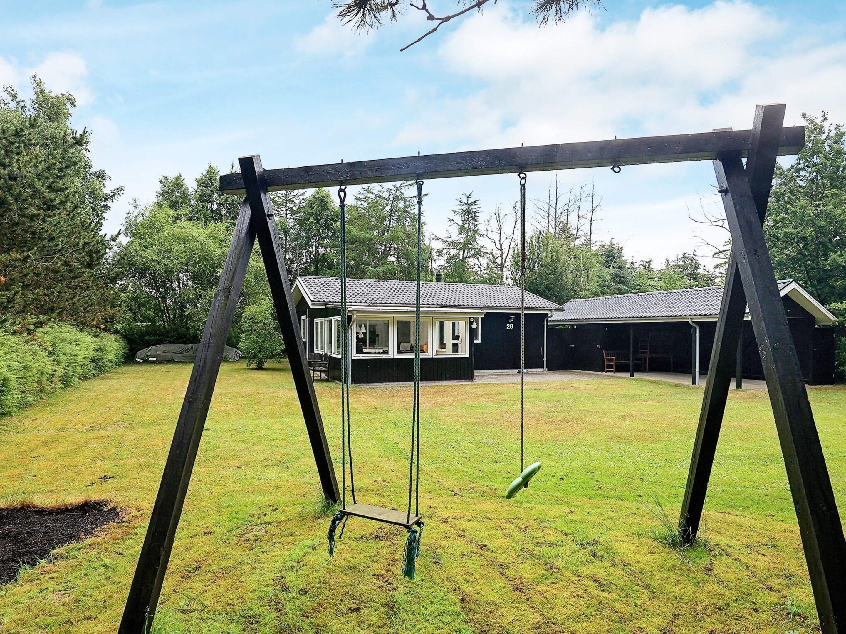 A wooden swing set in a grassy yard with a house in the background.