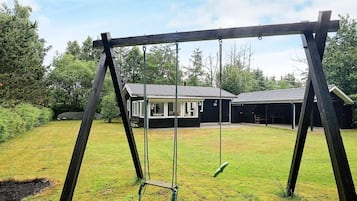 A wooden swing set in a grassy yard with a house in the background.