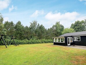 A black house with a porch and a swing set in a grassy yard. - 6 Person Holiday Home in Hals (Hals)