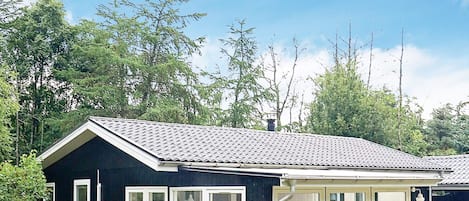 A small, dark-colored cabin with a tiled roof, large windows, and a bench outside.