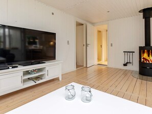A modern living room with a flat-screen TV, wooden flooring, a glass table with candles, and a wood-burning stove. - 6 Person Holiday Home in Hals (Hals)