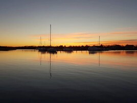 Una orilla tranquila con varias embarcaciones amarradas, reflejando el atardecer.