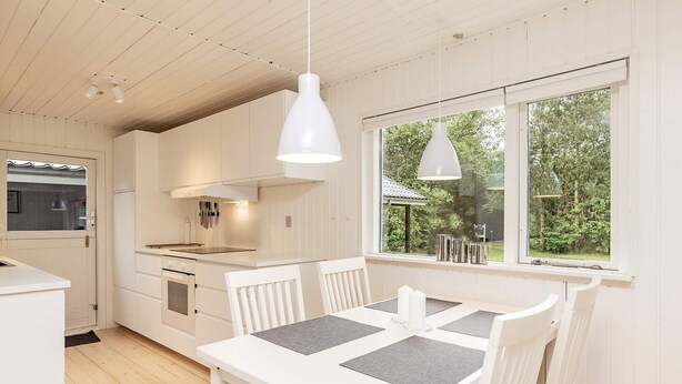 A modern kitchen with white cabinetry, a dining table with chairs, and a large window with a view of greenery.