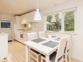 Una cocina moderna con armarios blancos, una mesa de comedor con sillas y un amplio ventanal con vistas a zonas verdes.