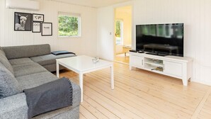 A modern living room with a grey sofa, a white coffee table, and a flat-screen TV on a white stand.