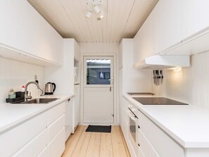A narrow kitchen with white cabinetry, a stainless steel sink, a kettle, and a window with a view.