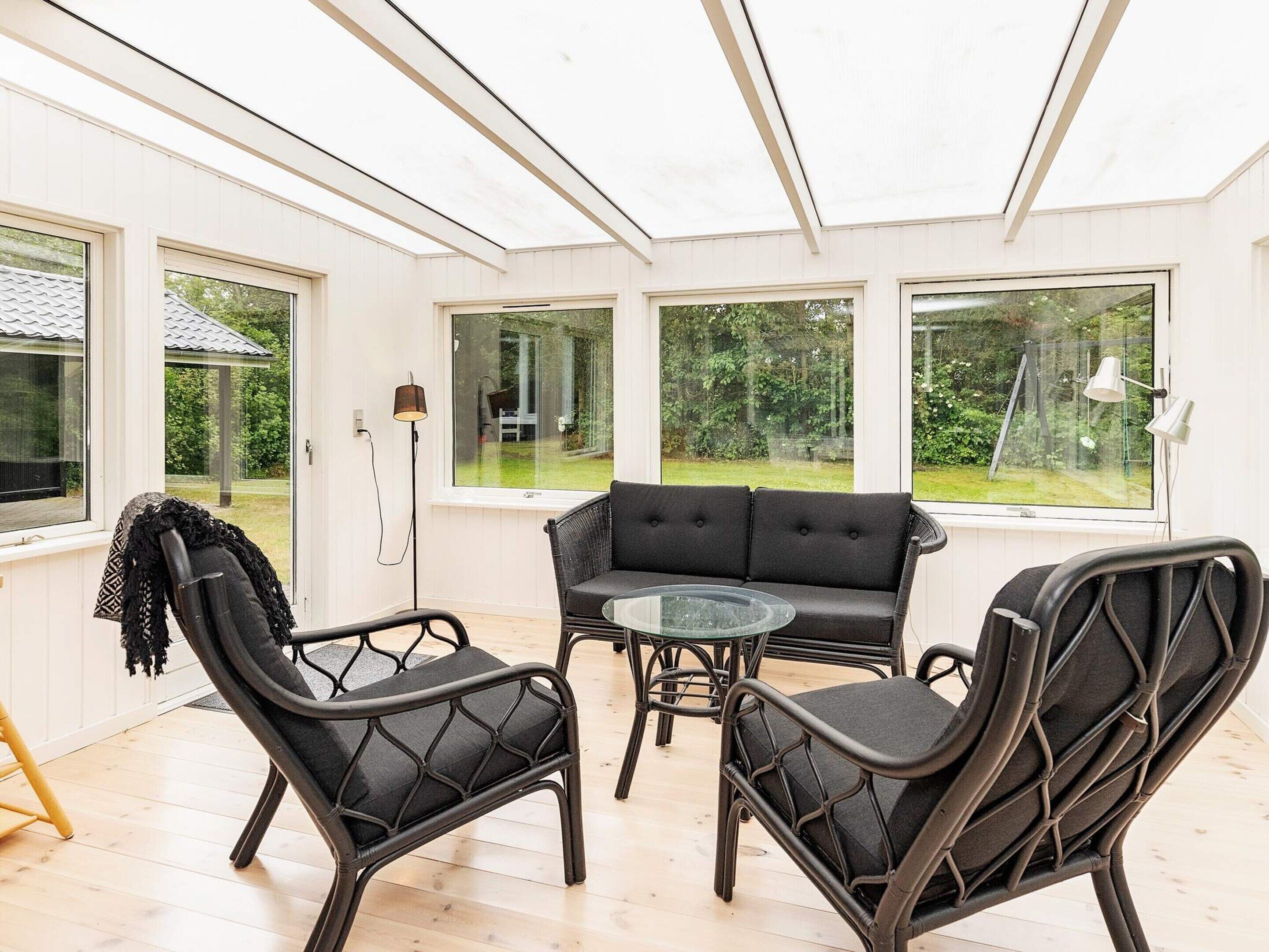 A conservatory with a sofa and chairs, large windows, and a lamp.