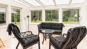 A conservatory with a sofa and chairs, large windows, and a lamp.