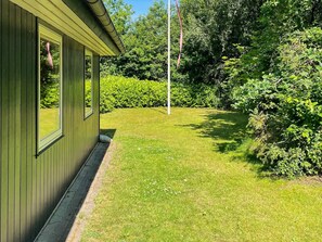 A green building with a well-maintained lawn and dense shrubbery. - 6 Person Holiday Home in Ansager (Ansager)