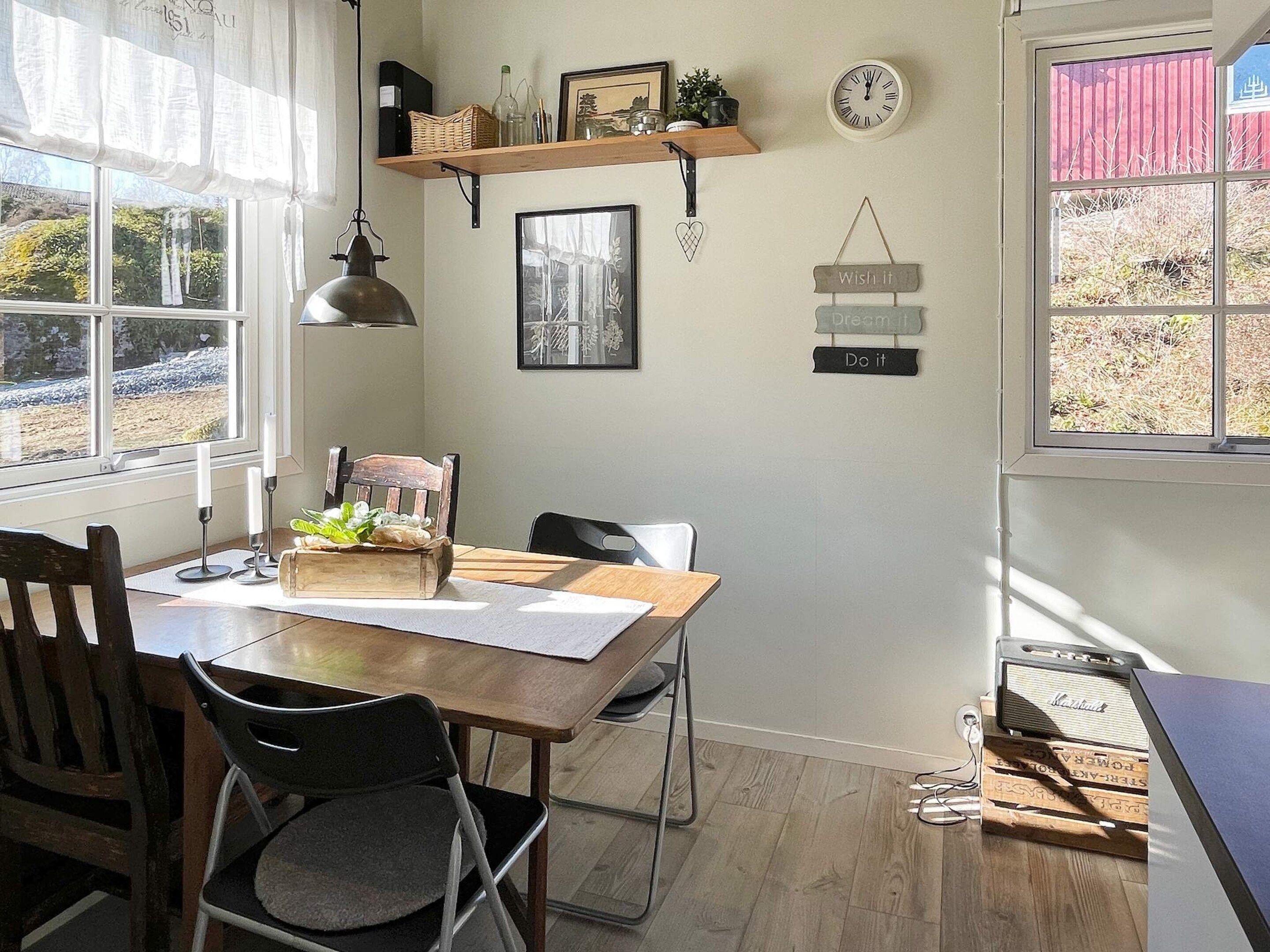 A dining area with a wooden table, chairs, a candle holder, a framed picture, a clock, and a shelf with decorative items.