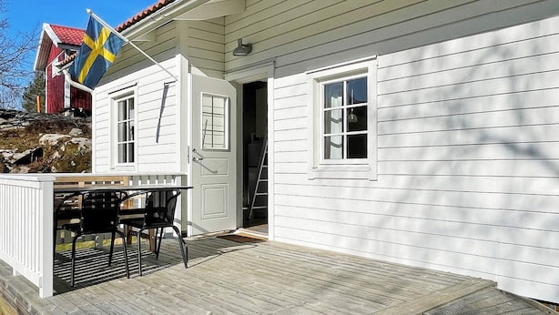 A white wooden house with a red roof, a flag, and a deck with chairs. - 6 Person Holiday Home in Hoviksnas (Höviksnäs)
