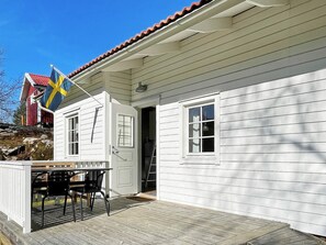 Une maison en bois blanche, avec un toit rouge, un drapeau et une terrasse avec des chaises.