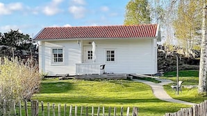 Une maison blanche avec un toit recouvert de tuiles rouges, un porche à l’avant et une pelouse bien entretenue.