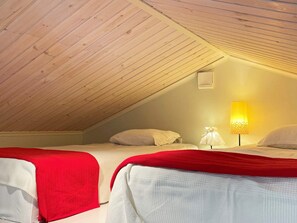 Una habitación con dos camas, techo inclinado, lámpara de pared y un ventanal pequeño.