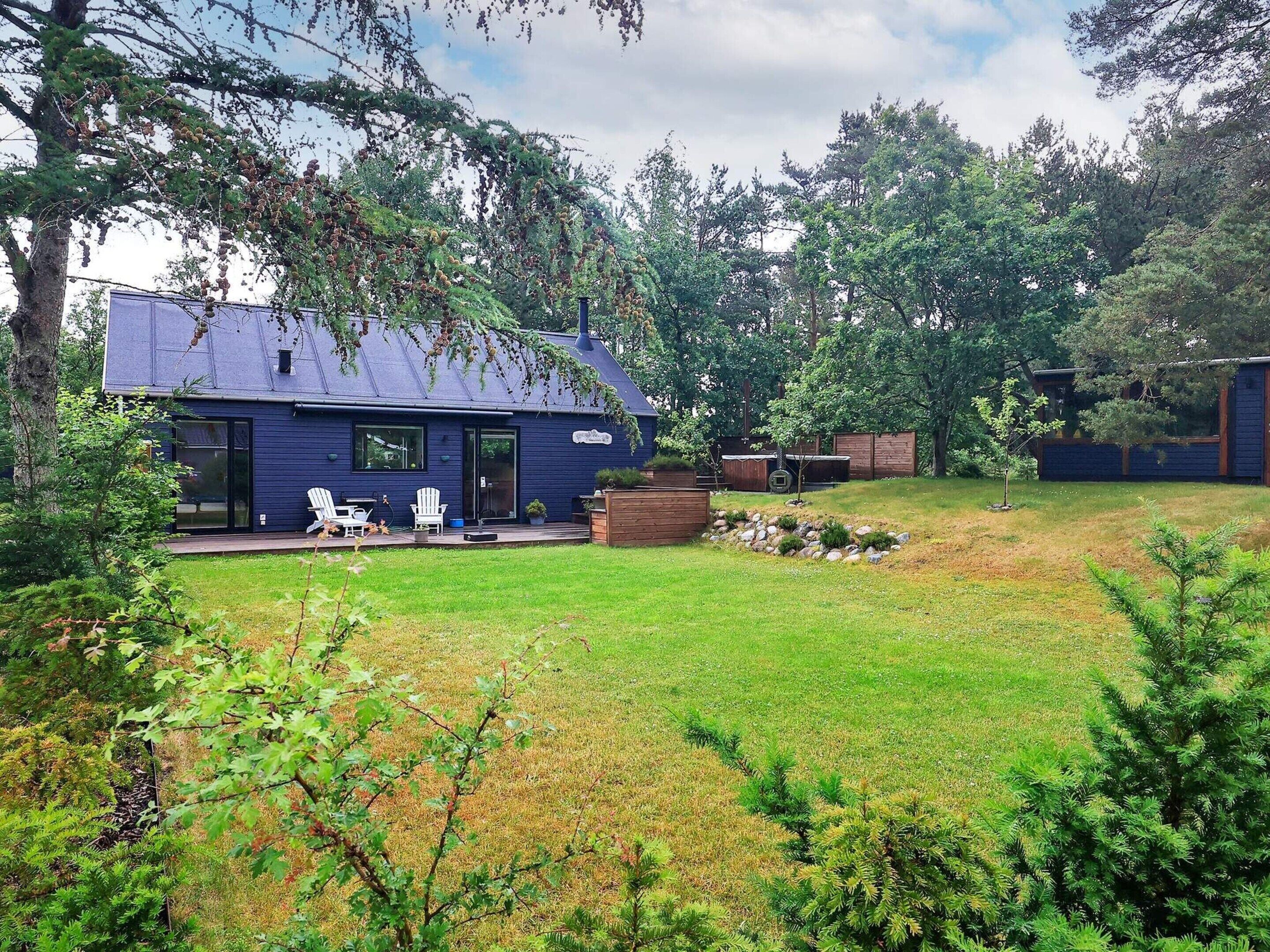A modern house with a blue exterior, a deck with outdoor seating, and a well-maintained lawn.