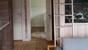 A room with a wooden floor, a white door, a gray sofa, and a painting of a mountain scene. - 7 Person Holiday Home in Orsta/brungot (Orsta)