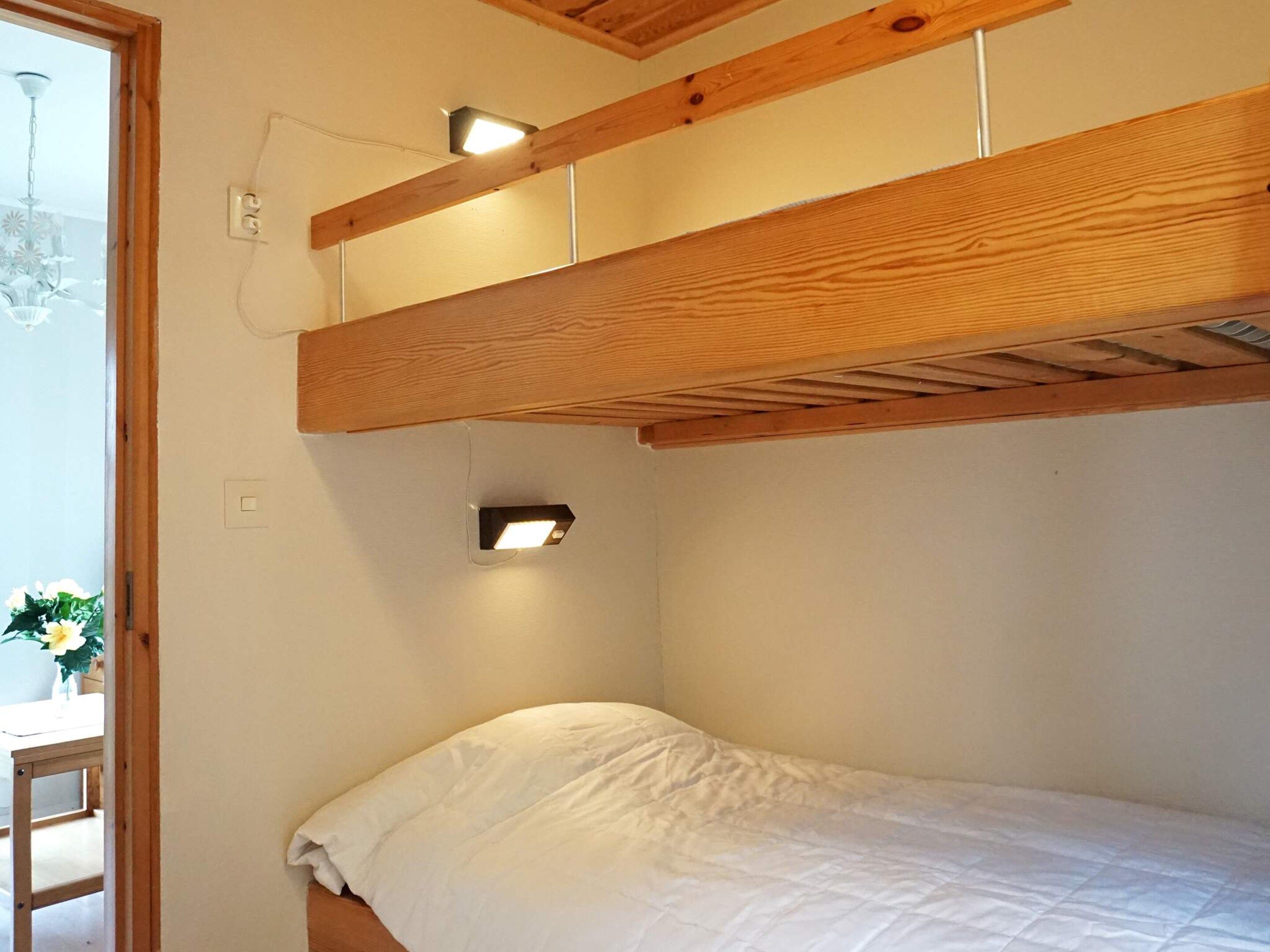 A bunk bed with a wooden headboard, a bedside table, and a wall-mounted light fixture.