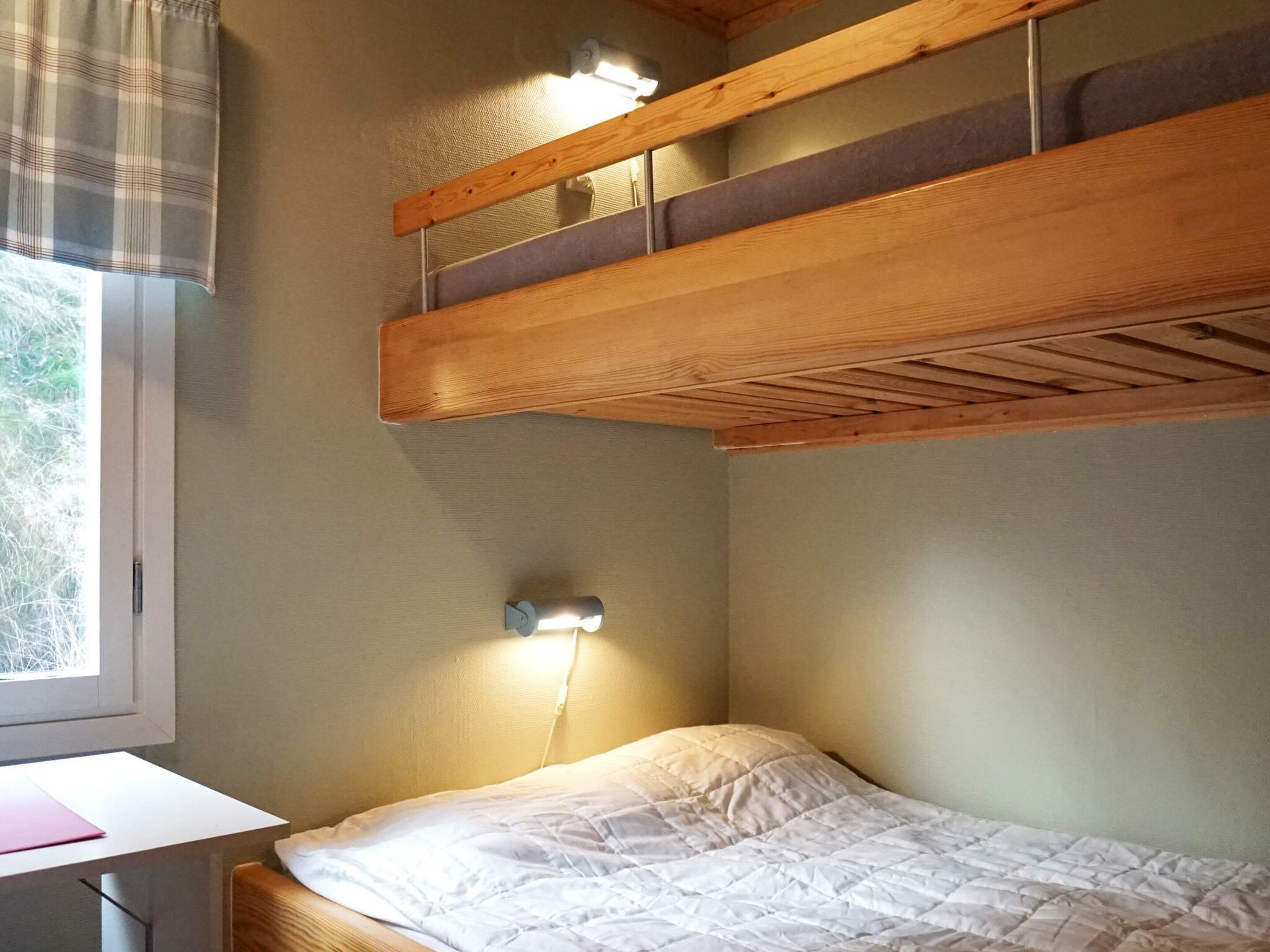 A room with a bunk bed, a desk, and a window.