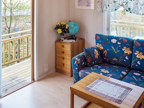 Une pièce dotée d’un plancher en bois, d’un canapé bleu à motifs floraux, d’une table d’appoint en bois, d’une commode en bois ornée d’un globe terrestre et de fleurs, et d’un balcon avec une rambarde.