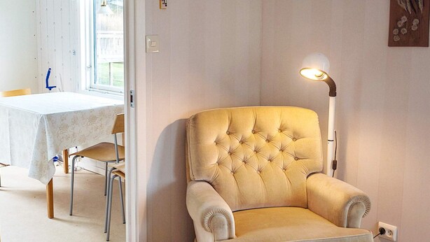 Quarto com poltrona estofada, mesa e cadeiras, e luminária de chão.