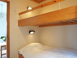 Un lit simple avec une tête de lit en bois et un luminaire fixé au mur.