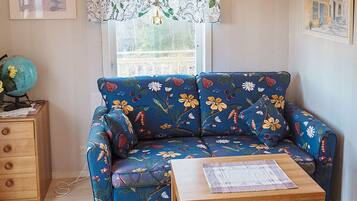 A room with a floral-patterned sofa, a wooden side table with a globe, and a window with a lace curtain.