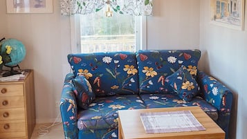 Um quarto com um sofá estampado com flores, uma mesa lateral de madeira, um globo e uma janela com cortina de renda.