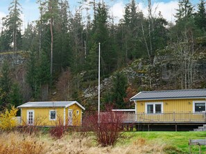 Two yellow buildings with a grassy foreground and a forested hillside in the background. - 4 Person Holiday Home in Hallevadsholm (Hällevadsholm)