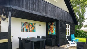 A covered outdoor patio with a dining table and chairs, a grill, and two colorful paintings on the wall.