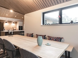 A modern kitchen with wooden ceiling, a dining area with a long table, chairs, and a vase.