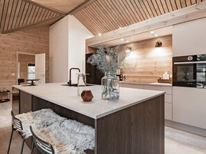 A modern kitchen with a central island, wooden ceiling, and built-in appliances.