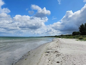 A beach with a sandy shore, calm water, and a partly cloudy sky.