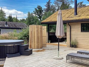 A wooden deck with a hot tub, outdoor seating, and a covered area with a thatched roof.