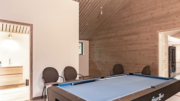 Una mesa de billar en una habitación con paredes y techo de madera, una ventana pequeña y una puerta.
