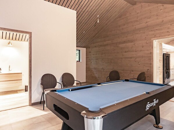 A pool table in a room with wooden walls and a ceiling, a small window, and a door.