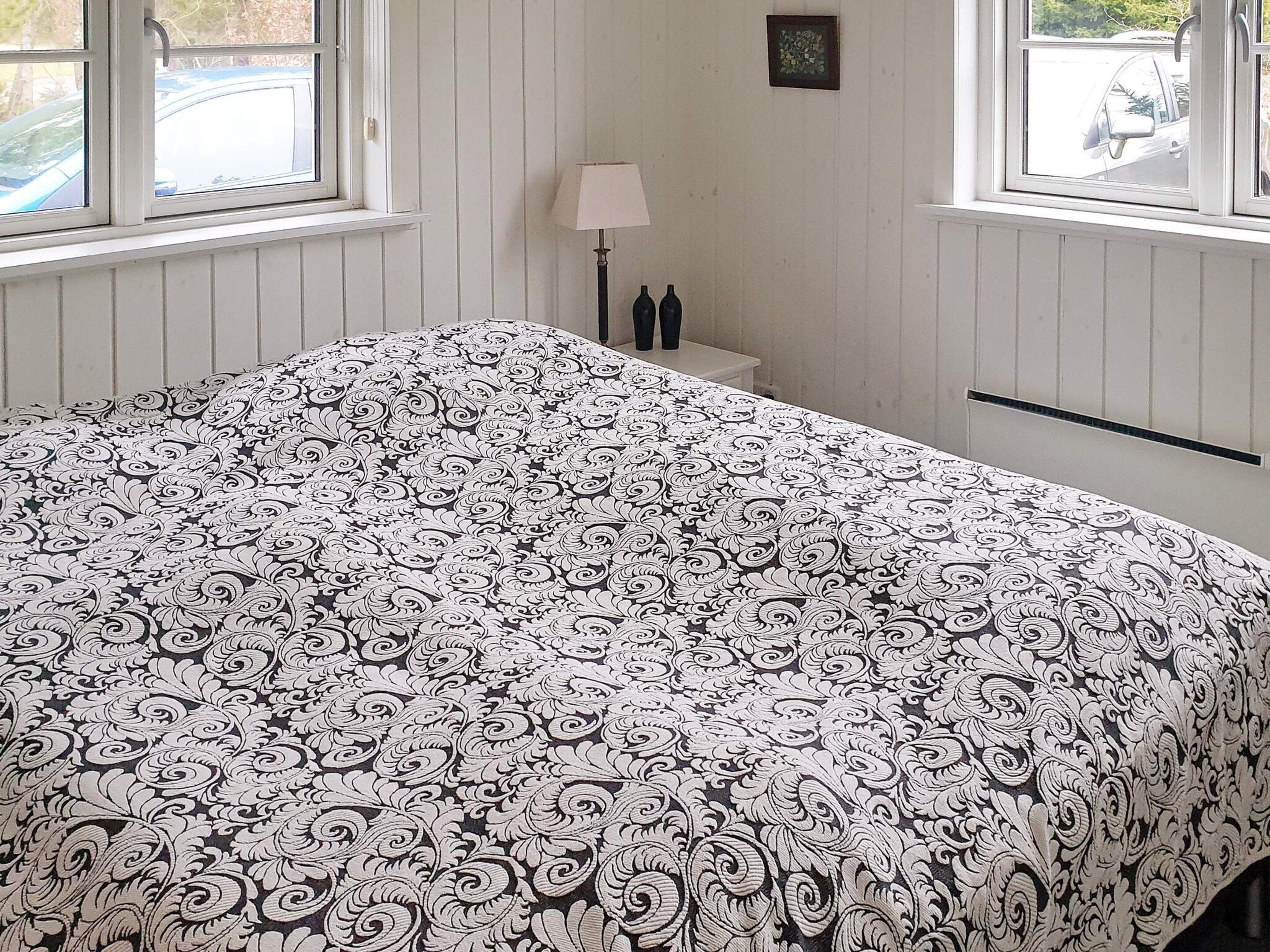 Una habitación con cama, una mesita de noche con lámpara y ventana con vista a un coche.