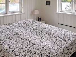 A room with a bed, a nightstand with a lamp, and a window with a view of a car.
