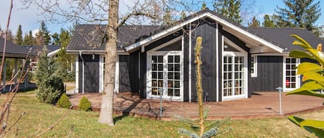 A modern two-story house with a large deck, surrounded by a well-maintained lawn and trees.