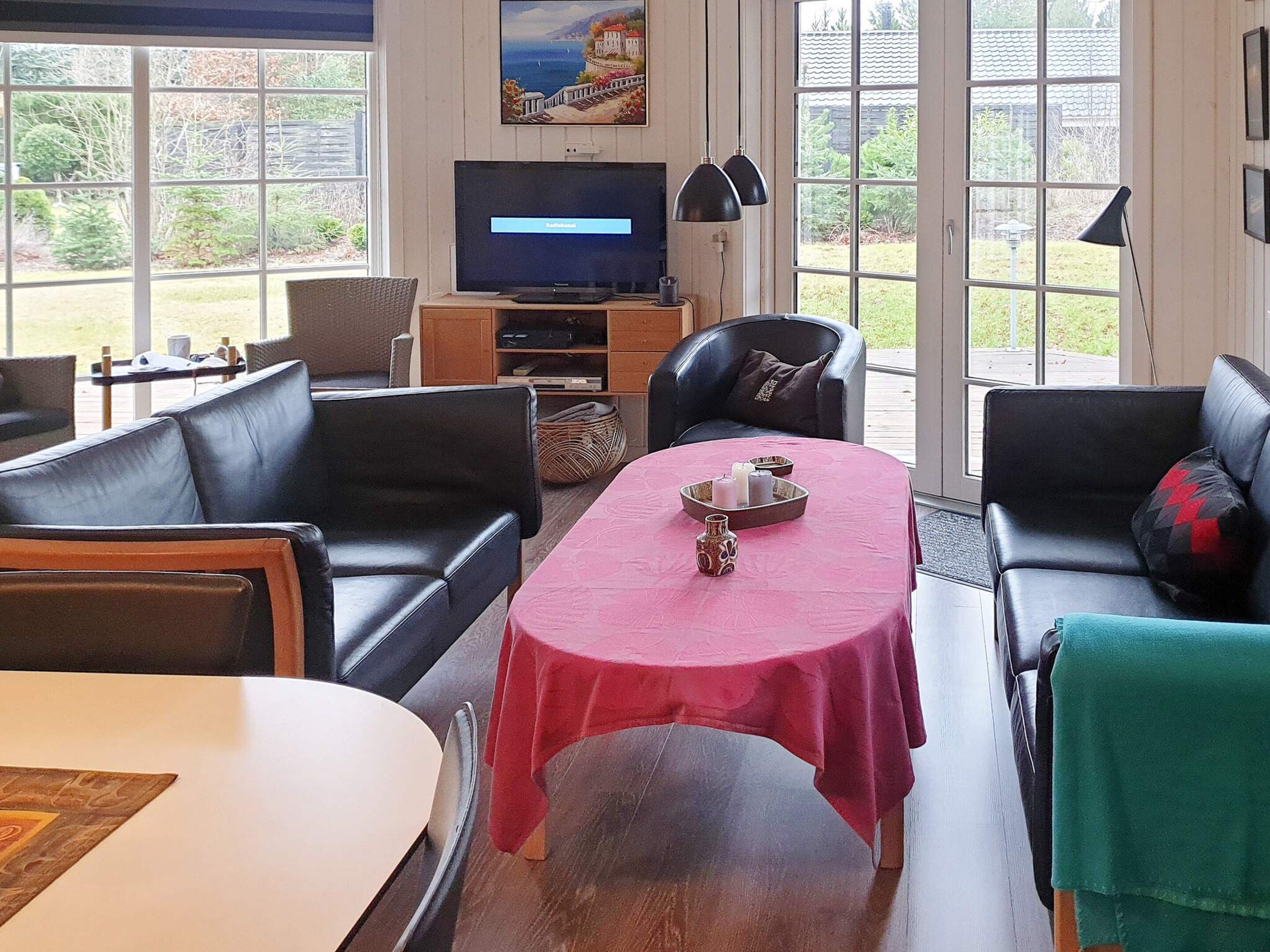 Una sala de estar con televisor, sofás de cuero, una mesa de comedor y vistas al exterior.