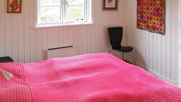 Una habitación con cama, una silla, un ventanal con persianas y una pared con colcha.