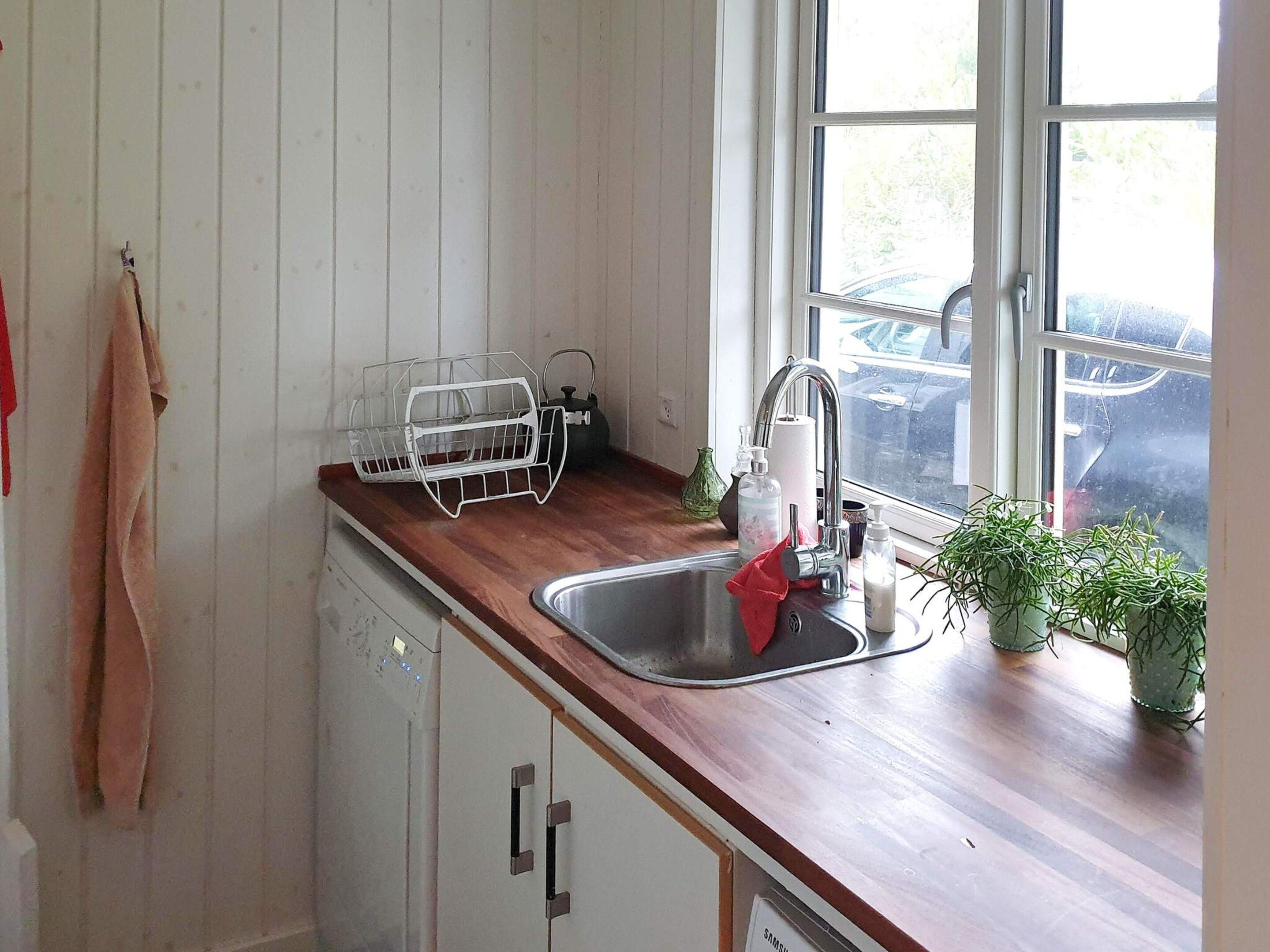 Una cocina con encimera de madera, un lavamanos de acero inoxidable, un escurreplatos y una ventana con vistas a coches estacionados.