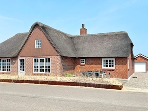 Une maison en briques avec un toit de chaume, une cheminée et un garage.