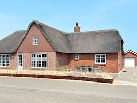 Une maison en briques avec un toit de chaume, une cheminée et un garage.