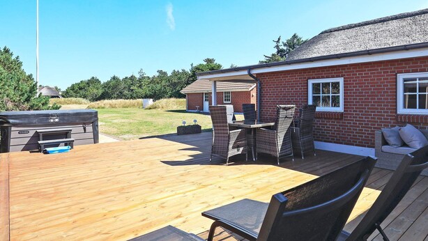 Une terrasse en bois avec des meubles d’extérieur, une maison en briques et une pelouse.