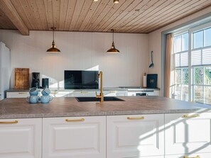 Une cuisine moderne avec des meubles blancs, un îlot central, une cuisinière noire et deux suspensions lumineuses.