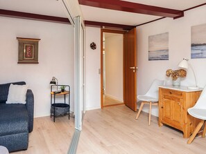 Una sala de estar moderna con un sofá gris, una mesita de noche con una lámpara, un mueble de madera y una puerta que da a otra habitación.