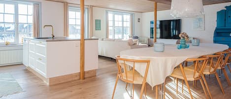A spacious kitchen with a central island, a dining area with a round table and chairs, and a large window providing natural light.