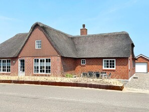 A single-story brick house with a steeply pitched thatched roof, a small chimney, and a garage. - 6 Person Holiday Home in Blavand (Blavand)