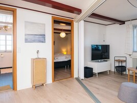A modern living room with a TV, a sofa, a small table, and a bed in the background.