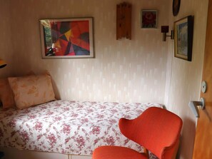 A bedroom with a bed, a chair, and a wall with three framed pictures.